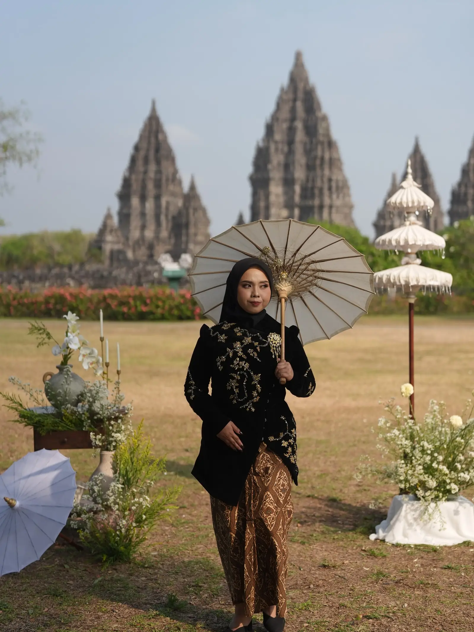 Dilla berkebaya hitam membawa payung kertas di Candi Prambanan