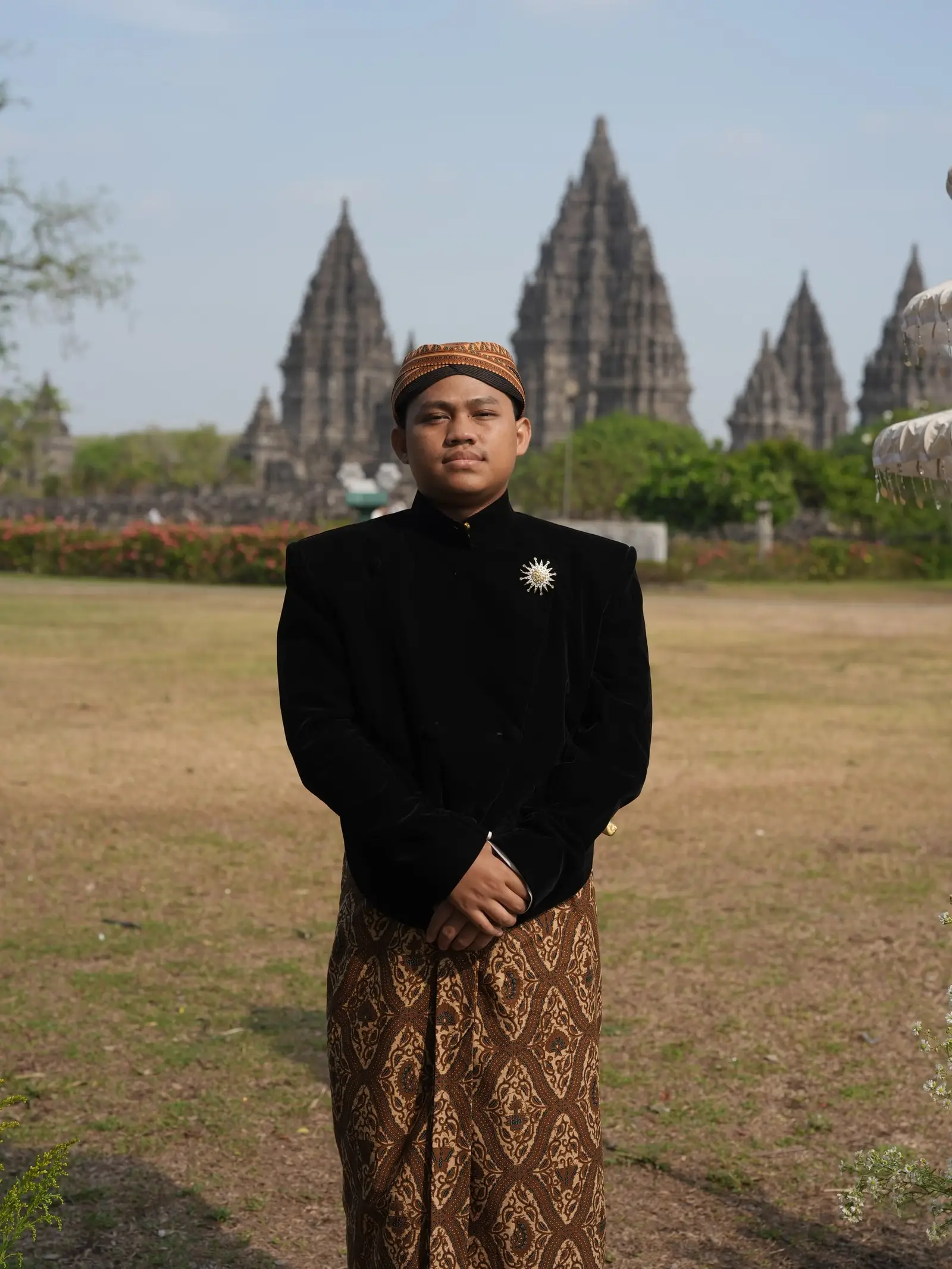 Nofan berbeskap hitam dan blangkon di depan Candi Prambanan