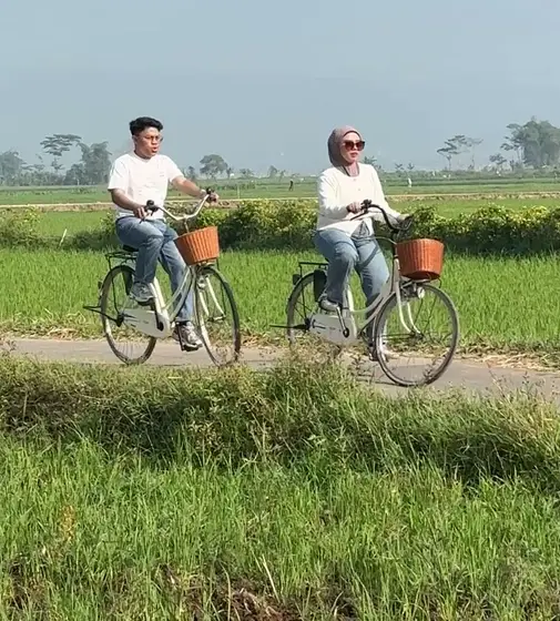 Dilla dan Nofan bersepeda di jalan tepi sawah