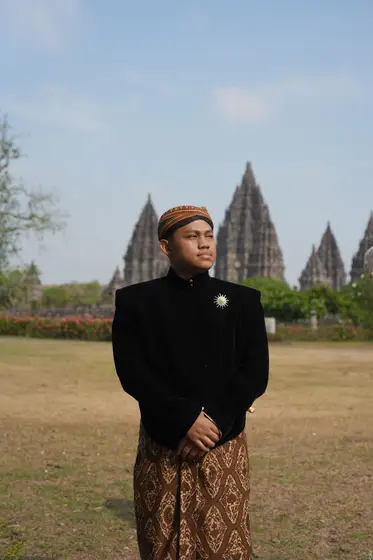 Nofan berbeskap hitam dan blangkon di depan Candi Prambanan